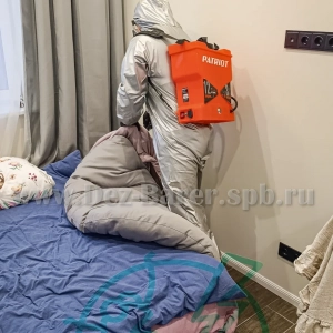Дезинфектор в защите обрабатывает кровать в спальне у окна